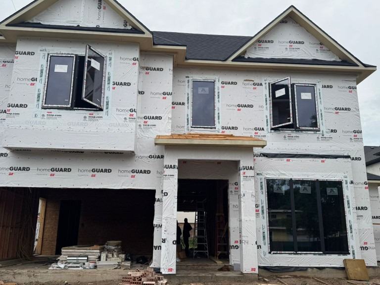 New construction house at dry-in with house wrap on and black Royal Windoor aluminum windows installed in the openings
