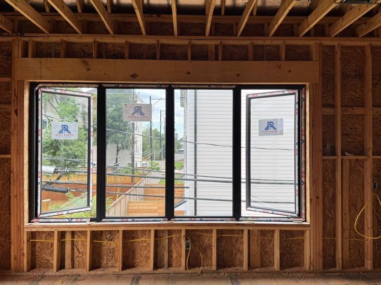 Four panel black aluminum Royal Windoor window unit installed in timber framing with factory labels still on the glass