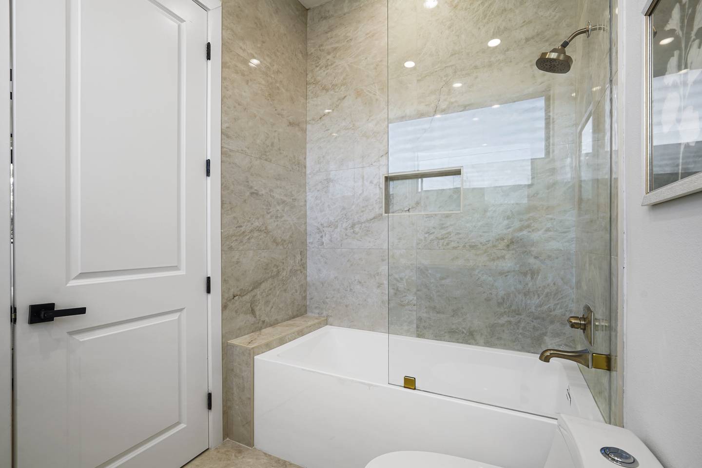 Semi-frameless glass shower panel over a tub in a marble bathroom
